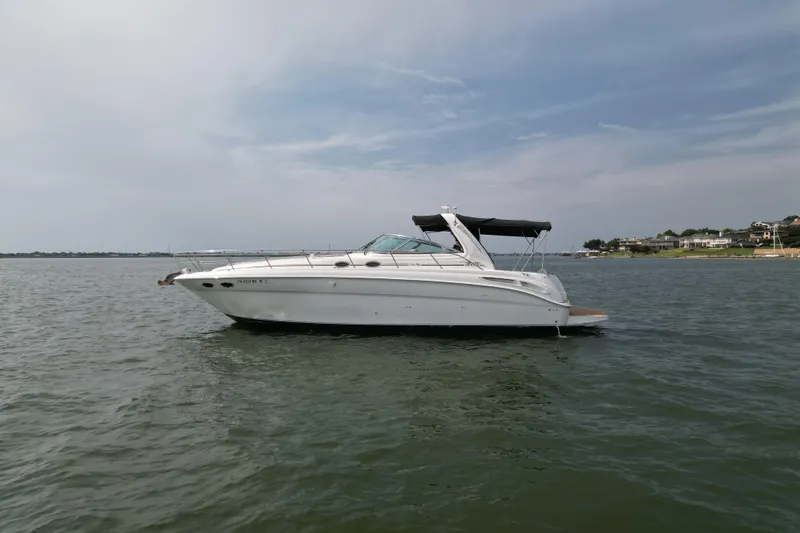 The Image of 2000 Sea Ray 380 Sundancer yacht on calm water, overcast sky, coastal background. - 0