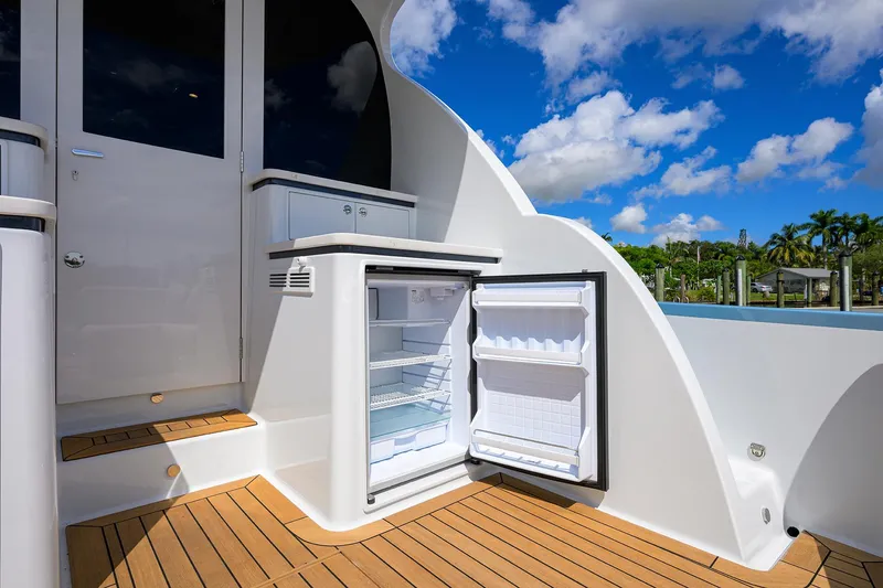 Slide: The Image of 2024 Palm Beach Motor Yachts GT50 with open deck fridge, wooden flooring, and scenic view. - 24