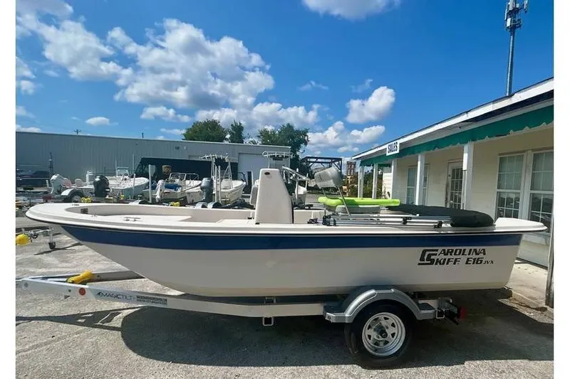 The Image of 2026 Carolina Skiff 16 JVX CC boat on trailer, parked outside dealership under blue sky. - 1