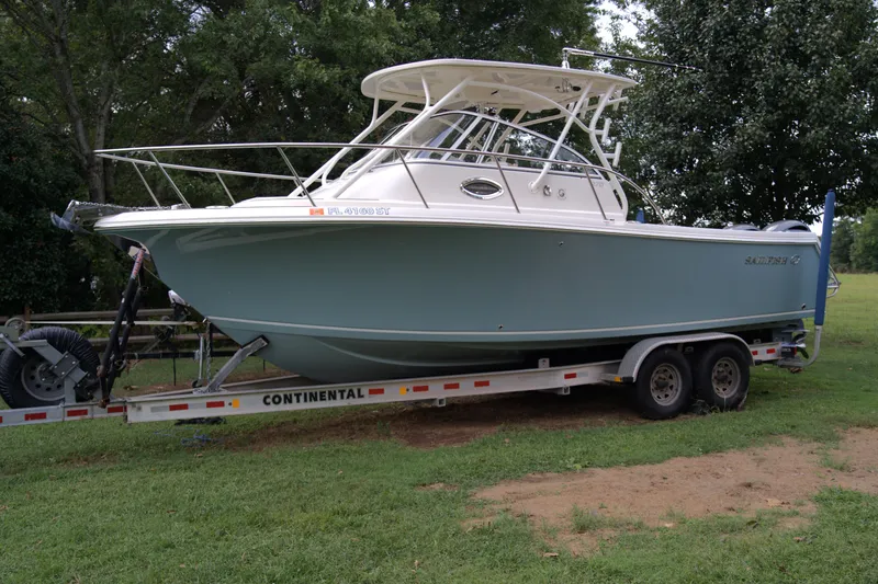 Slide: The Image of 2020 Sailfish 270 WAC boat on trailer, parked on grass with trees in background. - 3