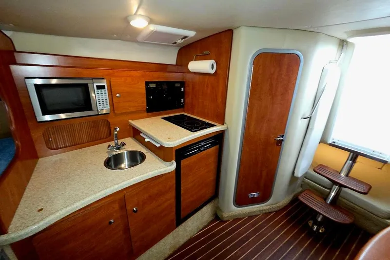Slide: The Image of 2007 Rinker 320 Express Cruiser interior kitchen with microwave, sink, and wooden cabinetry. - 3