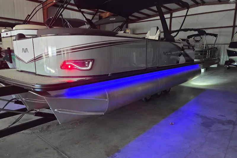 Slide: The Image of 2026 Avalon Platinum LSZ 2385 Quad Lounger pontoon boat with blue LED lights in a showroom. - 14
