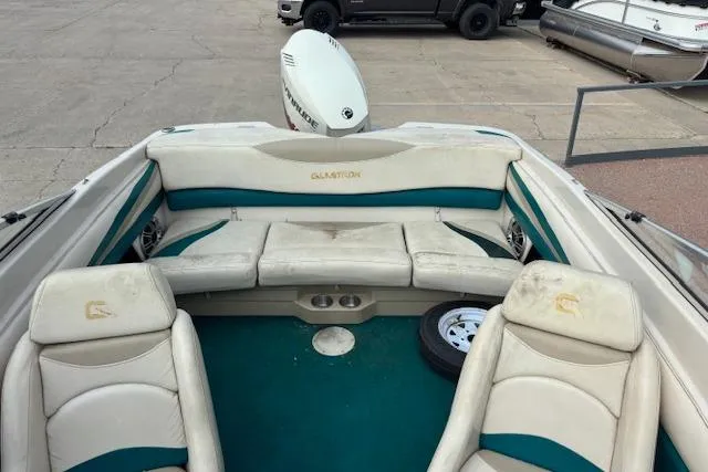 Slide: The Image of 2000 Glastron GX 180 boat interior with white and teal seating, parked on concrete. - 16