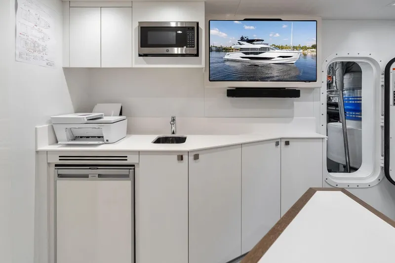 Slide: The Image of Modern yacht interior with kitchenette, TV displaying Sunseeker 90 Ocean 2024 model, and office equipment. - 71