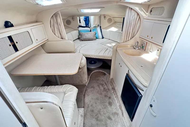 Slide: The Image of Interior of 2000 Sea Ray 290 Sundancer, featuring cozy seating, kitchenette, and sleeping area. - 11