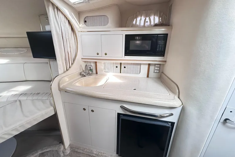 Slide: The Image of Compact kitchen area in a 2000 Sea Ray 290 Sundancer boat, featuring sink, microwave, and storage. - 13