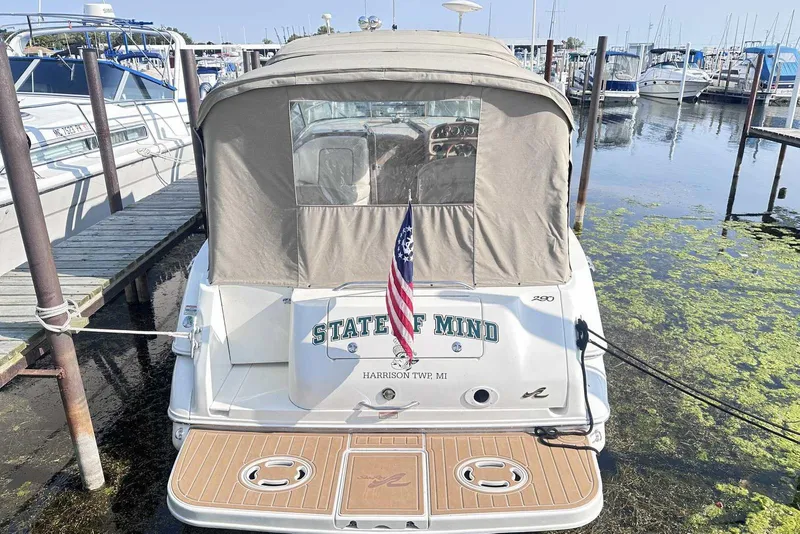 Slide: The Image of 2000 Sea Ray 290 Sundancer docked, rear view with American flag and covered cockpit. - 2
