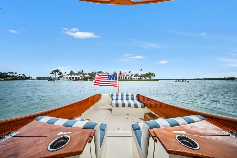 Slide: The Image of 2019 Hinckley Picnic Boat 34 on water, American flag, striped seating, scenic view. - 3