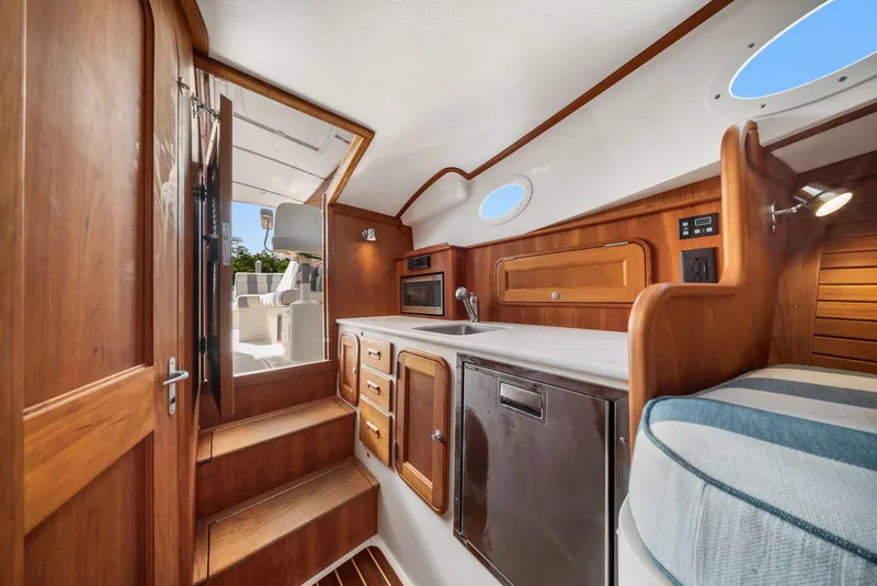 Slide: The Image of 2019 Hinckley Picnic Boat 34 interior with wood cabinetry, compact kitchen, and cozy seating. - 9