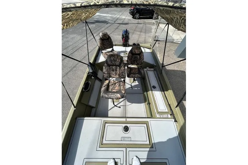 Slide: The Image of 2024 Lund 1660 Predator Tiller boat with camo seats and canopy, parked outdoors. - 10