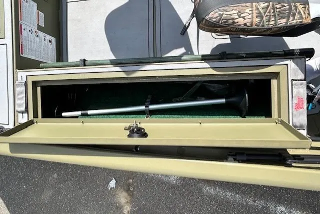 Slide: The Image of 2024 Lund 1660 Predator Tiller boat storage compartment with fishing rod and equipment. - 13