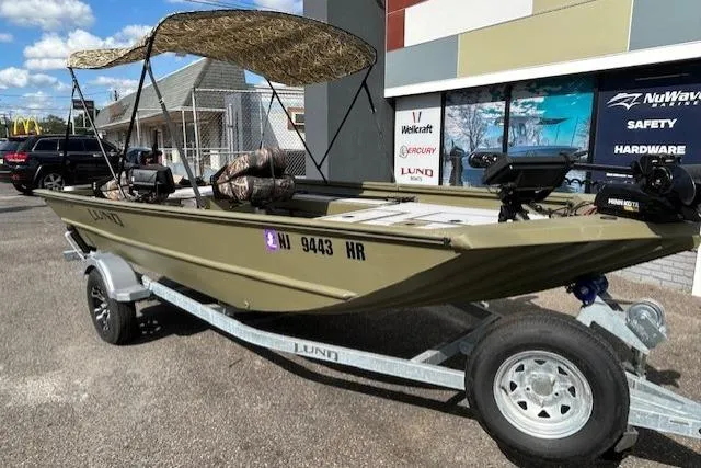 Slide: The Image of 2024 Lund 1660 Predator Tiller boat on trailer, featuring canopy and outdoor setting. - 2
