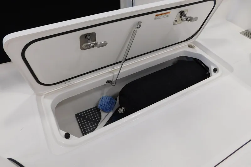 Slide: The Image of Open storage compartment on 2022 Pursuit S 328 Sport boat, featuring cleaning brush and mat. - 17