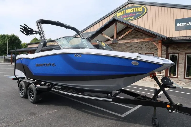 The Image of 2026 MasterCraft NXT22 boat in showroom, blue and white design on trailer. - 1