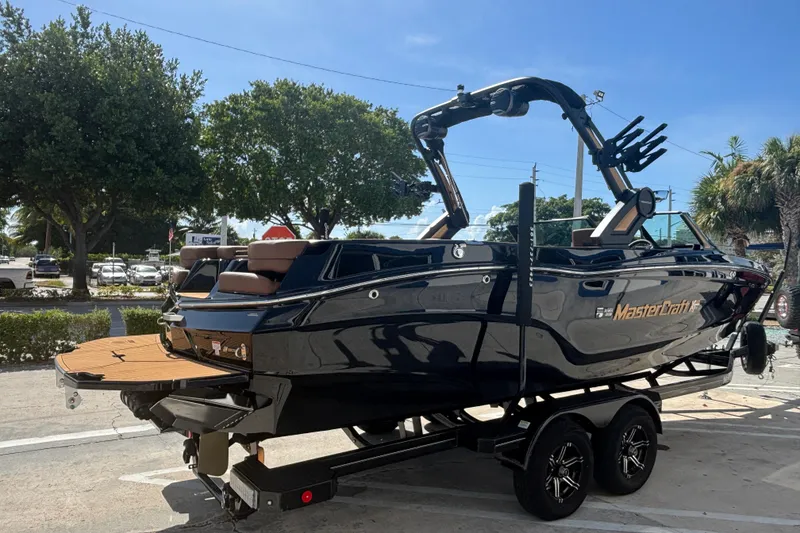 Slide: The Image of 2026 MasterCraft XT24 boat on trailer, sleek black design, parked outdoors. - 2