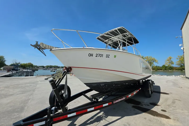 Slide: The Image of 2006 Boston Whaler 240 Outrage boat on trailer, parked near waterfront under clear blue sky. - 3