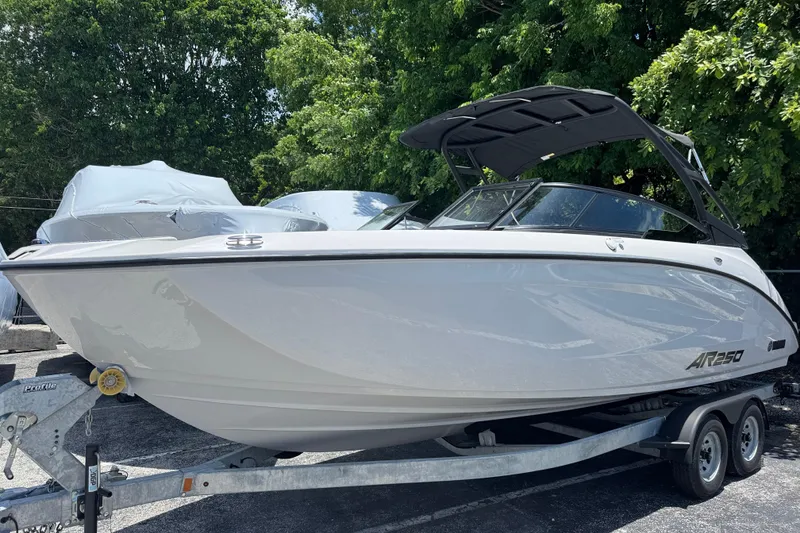 The Image of 2025 Yamaha Boats AR250 on trailer, sleek design, parked outdoors with trees in background. - 1