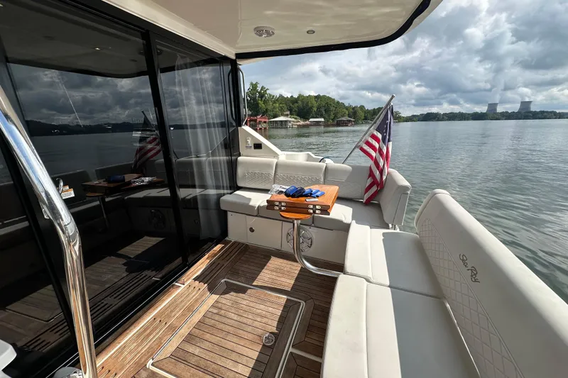 Slide: The Image of 2017 Sea Ray Fly 460 yacht deck with seating, table, and American flag on a serene lake. - 12