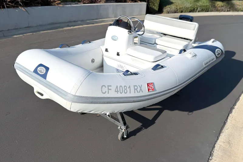 Slide: The Image of 2015 Walker Bay Genisis 310 inflatable boat on pavement, featuring steering console and seating. - 19