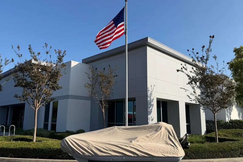 Slide: The Image of Covered Walker Bay Genisis 310 boat, 2015 model, near modern building with American flag. - 4