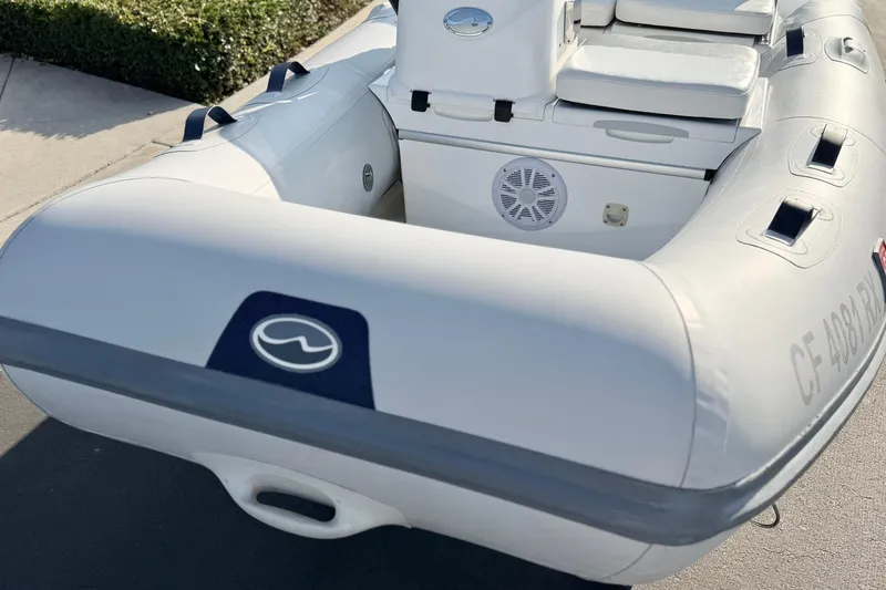 Slide: The Image of 2015 Walker Bay Genisis 310 inflatable boat, white with seating and speaker, docked outdoors. - 9