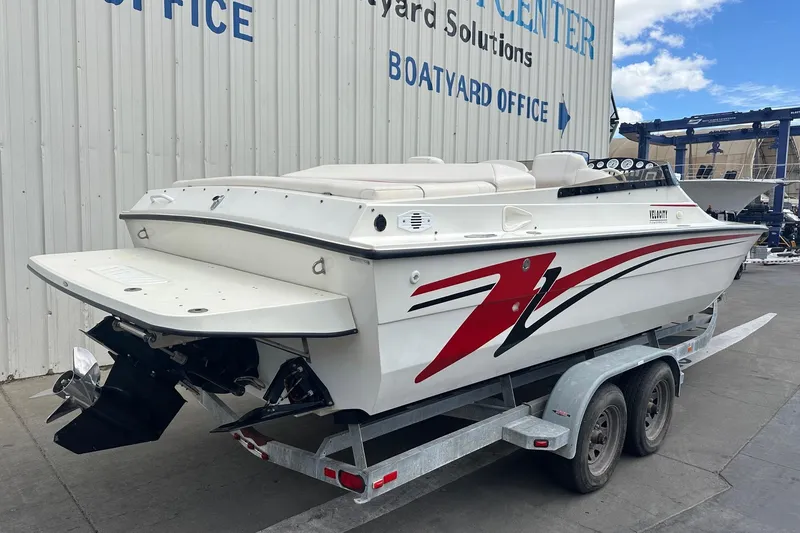 Slide: The Image of 1998 Velocity 26 Thoroughbred boat on trailer, white with red accents, at a boatyard. - 2