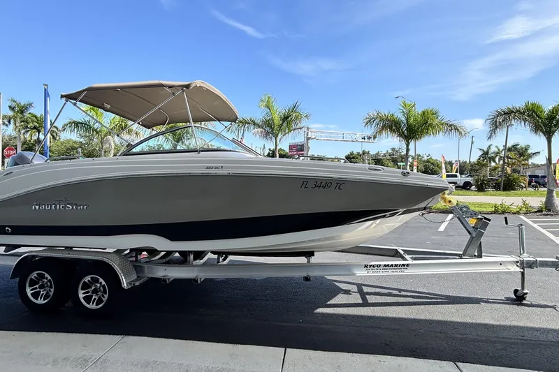 Slide: The Image of 2015 NauticStar 223 DC boat on trailer, parked with palm trees in background. - 2