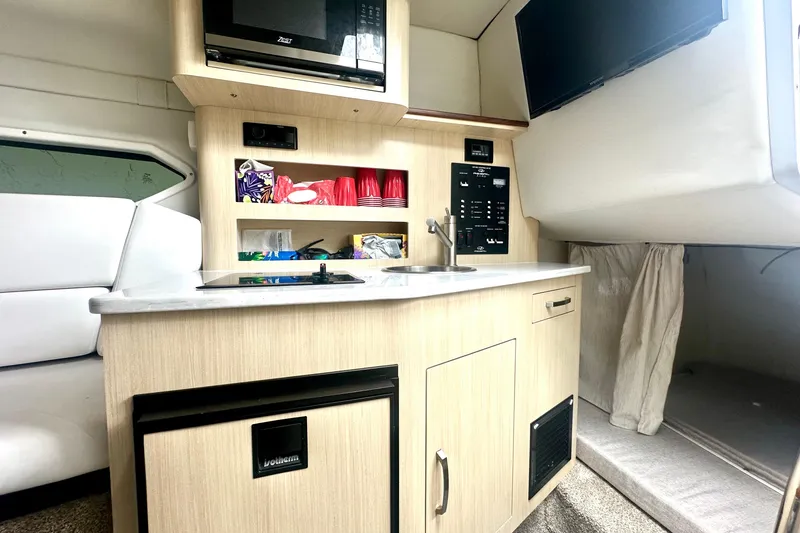 Slide: The Image of 2025 Regal 26 XO boat interior with kitchenette, microwave, and TV. - 49