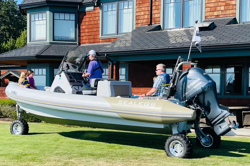 Slide: The Image of 2022 Sealegs 7.5M amphibious boat on grass, near a house, with passengers onboard. - 2