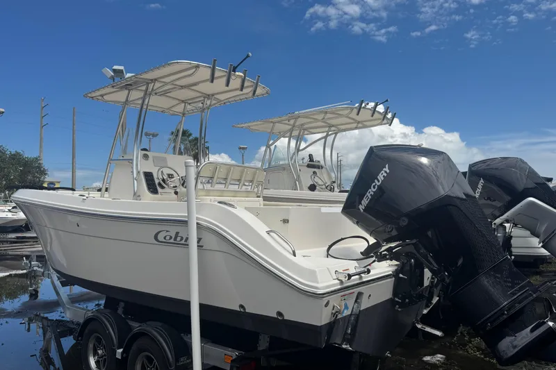 Slide: The Image of 2022 Cobia 237 Center Console boat with Mercury engines, parked on a trailer under a clear blue sky. - 2