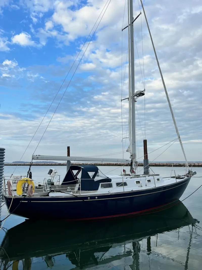 The Image of 1967 Jensen Cal 36 sailboat docked under a partly cloudy sky. - 0