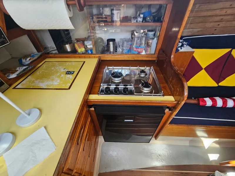 Slide: The Image of 1967 Jensen Cal 36 yacht kitchen with stove, wooden cabinetry, and colorful cushions. - 32