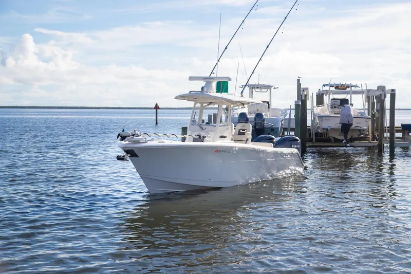 Slide: The Image of 2023 Cobia 280 Center Console boat docked on calm water under a clear sky. - 16