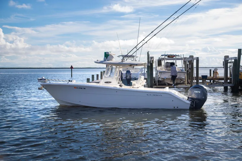 Slide: The Image of 2023 Cobia 280 Center Console boat docked on calm water with fishing rods. - 20
