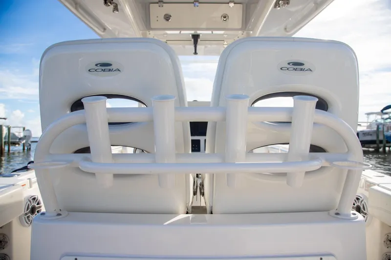 Slide: The Image of 2023 Cobia 280 Center Console boat seats with rod holders, docked under clear skies. - 28