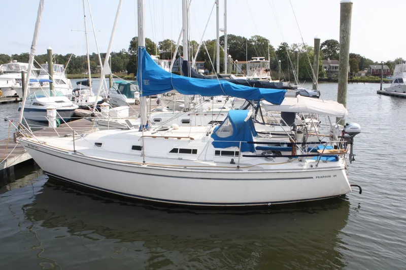 The Image of 1988 Pearson 31 sailboat docked at marina with blue covers and calm water. - 0