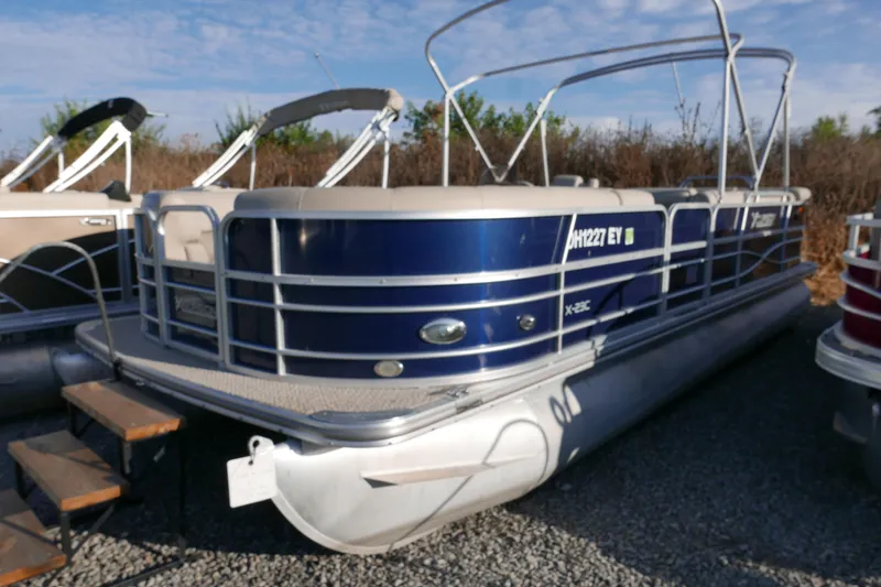 Slide: The Image of 2012 Xcusrion x2312 pontoon boat with blue exterior, docked on gravel. - 2