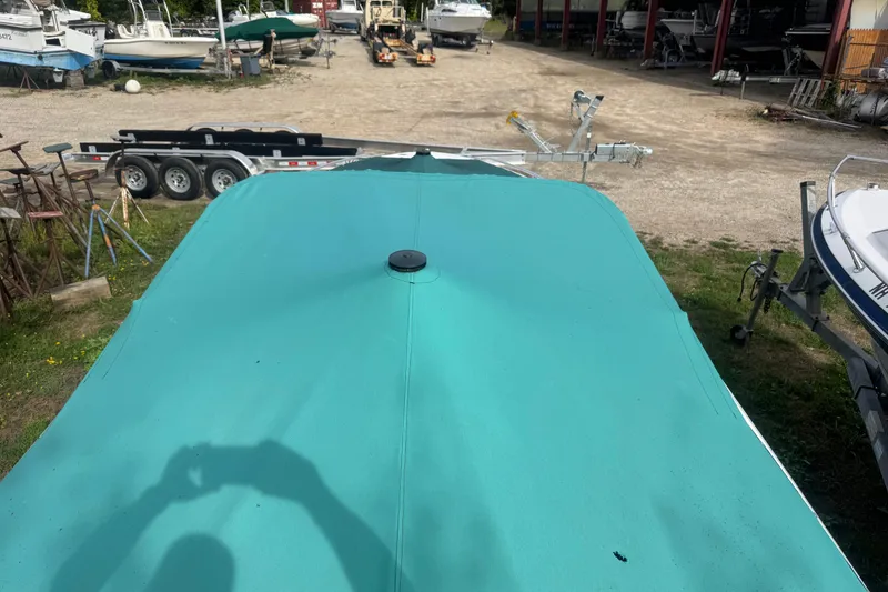 Slide: The Image of 1991 Sea Ray 220 boat with teal cover in a boatyard setting. - 12