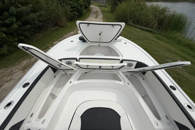 Slide: The Image of 2026 Tidewater 2700 Carolina Bay boat with open storage compartments, docked near lush greenery. - 42