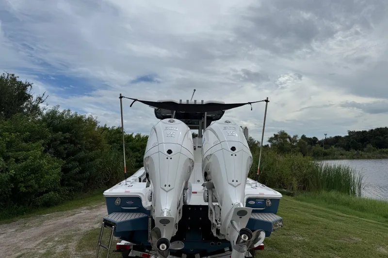 Slide: The Image of 2026 Tidewater 2700 Carolina Bay boat with dual engines, parked near a lake under cloudy skies. - 53