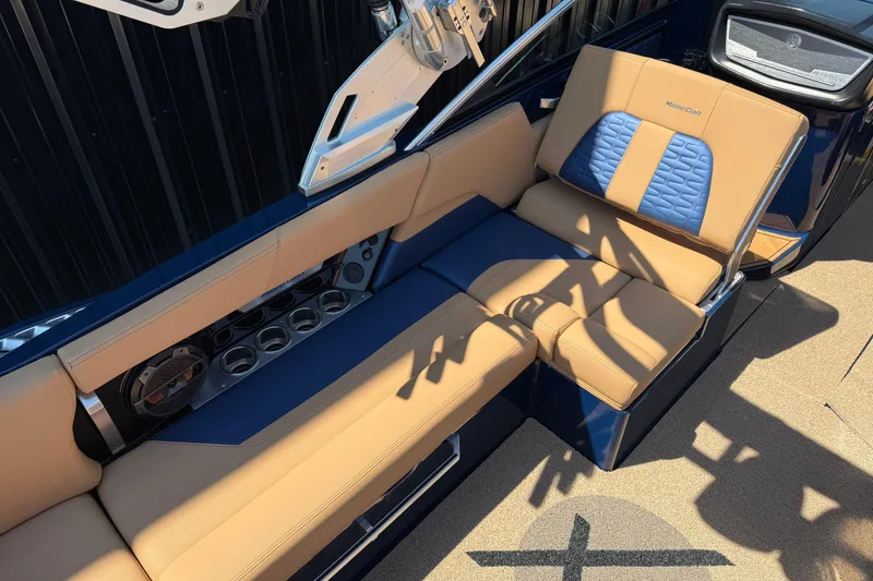 Slide: The Image of 2019 MasterCraft X26 boat interior with tan and blue seating, cup holders, and speaker system. - 2