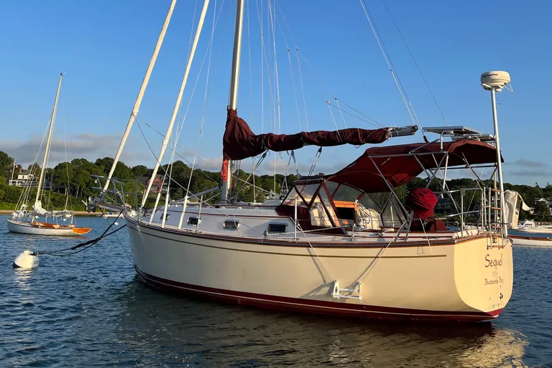 Slide: The Image of 1989 Island Packet 31 sailboat anchored in a serene bay, under clear blue skies. - 0