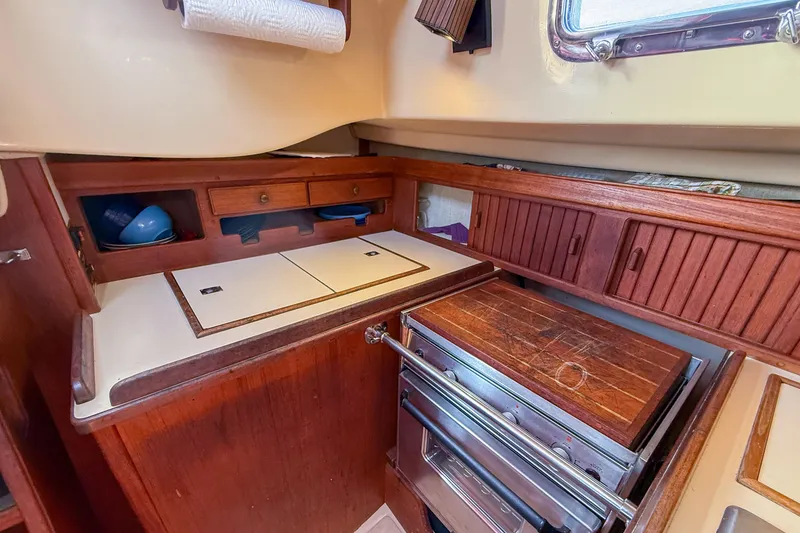 Slide: The Image of 1989 Island Packet 31 yacht galley with wooden cabinetry, stove, and storage compartments. - 19