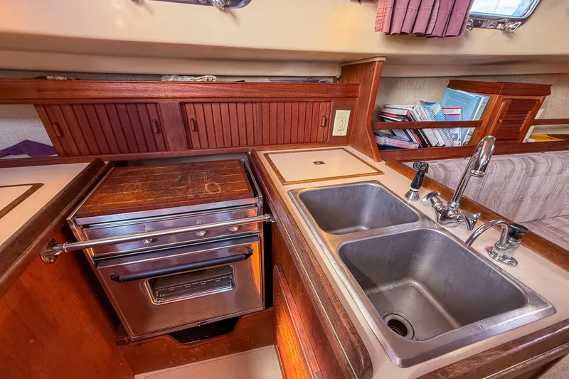 Slide: The Image of 1989 Island Packet 31 yacht kitchen with dual sinks, stove, and wooden cabinetry. - 22