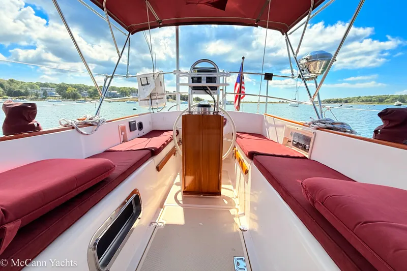 Slide: The Image of 1989 Island Packet 31 sailboat cockpit with red cushions, steering wheel, and scenic water view. - 4
