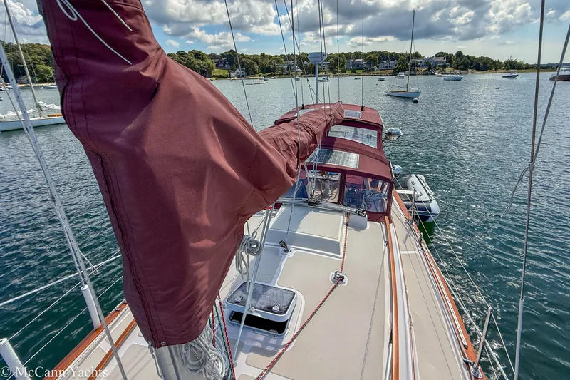 Slide: The Image of 1989 Island Packet 31 sailboat with maroon sails docked in a scenic harbor. - 51