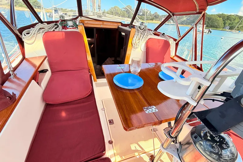 Slide: The Image of 1989 Island Packet 31 sailboat cockpit with red cushions, wooden table, and nautical equipment. - 7