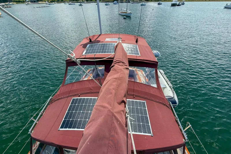 Slide: The Image of 1989 Island Packet 31 sailboat with solar panels on deck, anchored in a serene harbor. - 8
