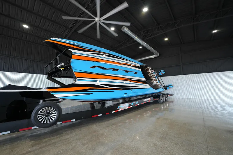 Slide: The Image of 2025 MTI 440X speedboat in a garage, featuring vibrant blue and orange design. - 2