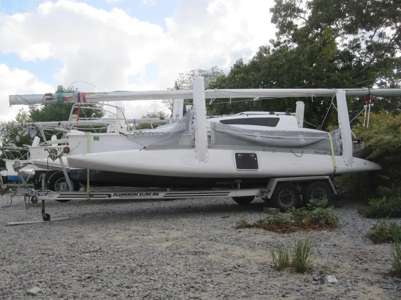 Slide: The Image of 2010 Corsair Dash 750 sailboat on trailer, parked on gravel, surrounded by trees. - 2